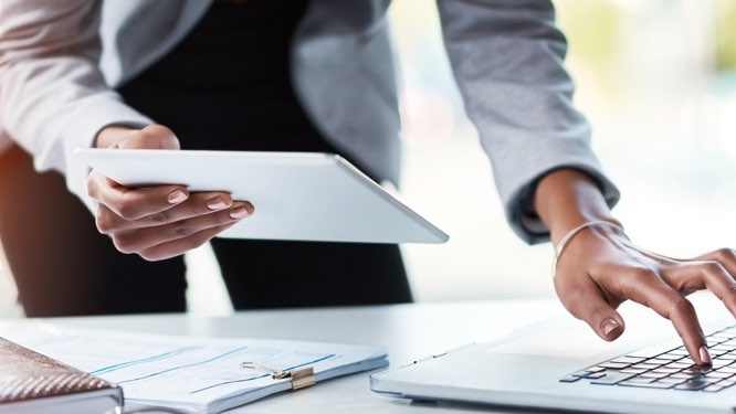 view of a person holding a tablet in one hand and working on a laptop keyboard with the other